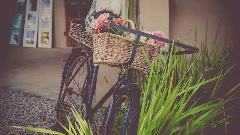 Fahrrad mit Blumen im Weidenkorb am Straßenrand.