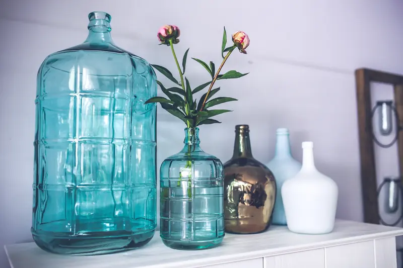 Türkisfarbene Glasflaschen mit einzelnen Blüten auf einer Kommode.