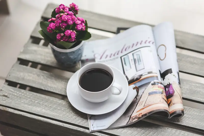 Pinkfarbene Topfblume neben einer Tasse Kaffee auf einem Holztisch.